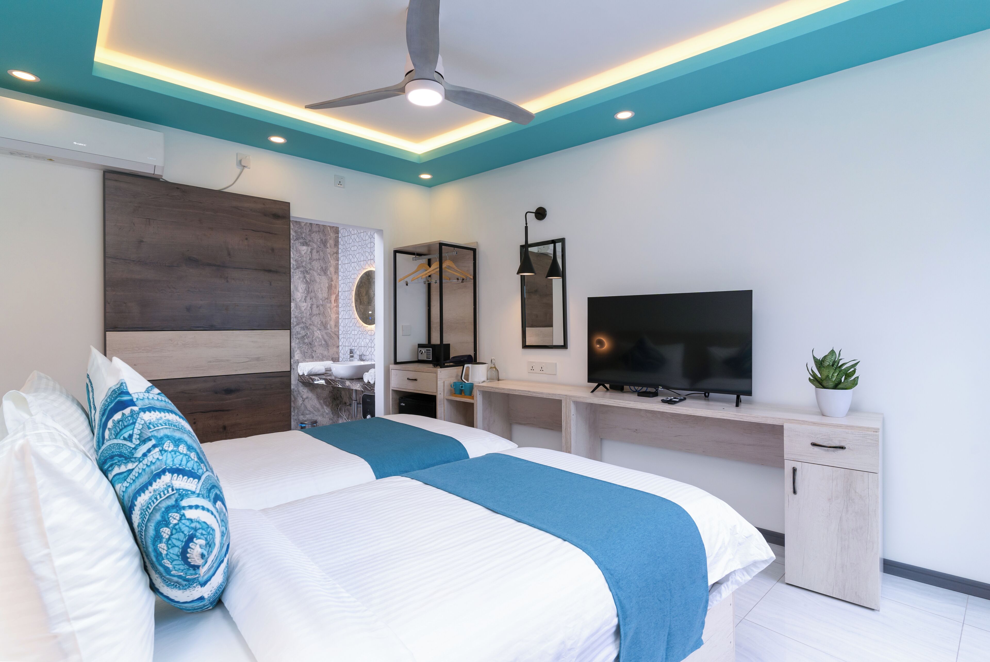 Una camera d'albergo moderna con un letto, una scrivania, una TV e una ventola a soffitto.