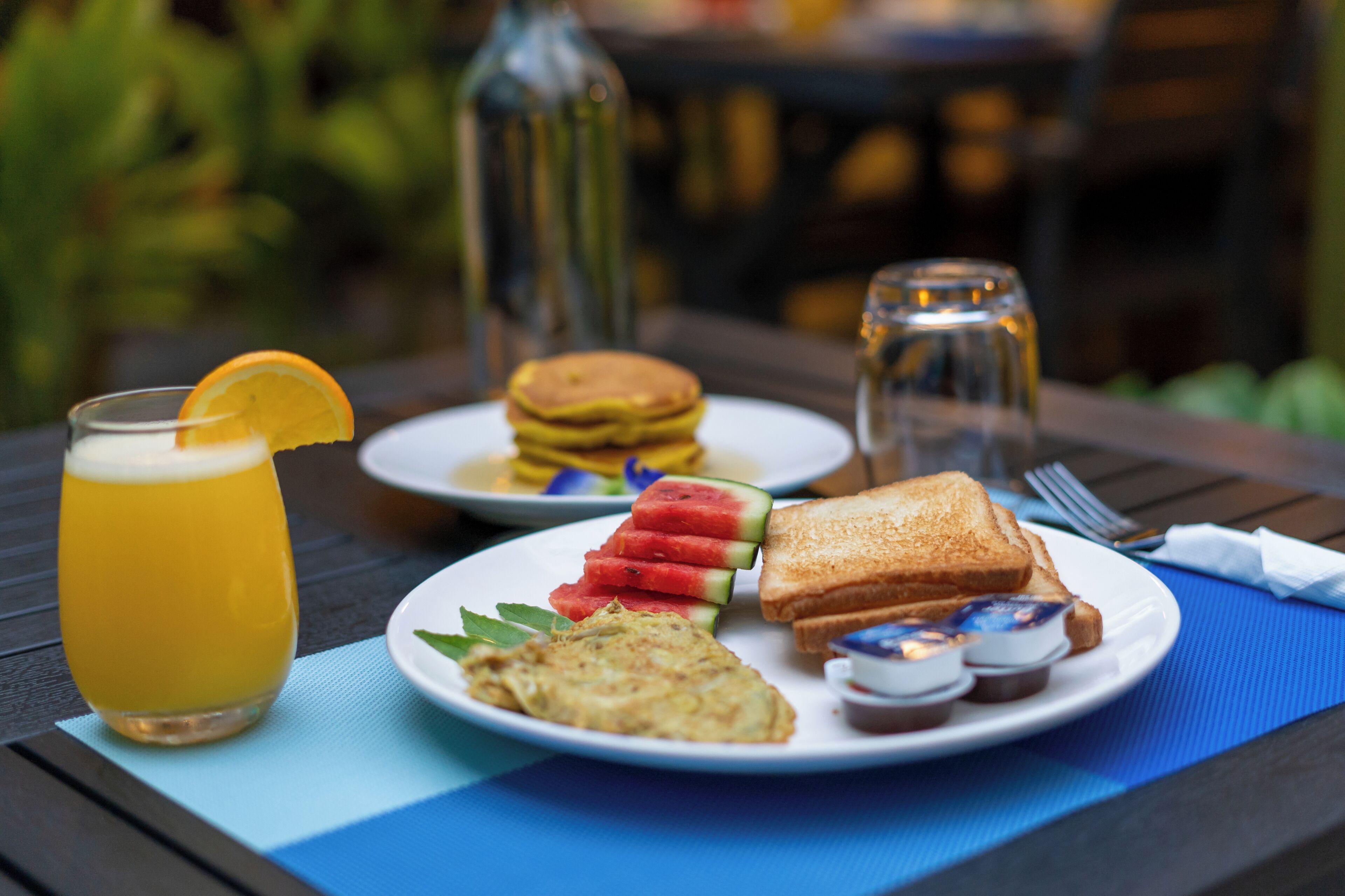A breakfast setting with a glass of orange juice, toast, pancakes, and a plate of fruit.