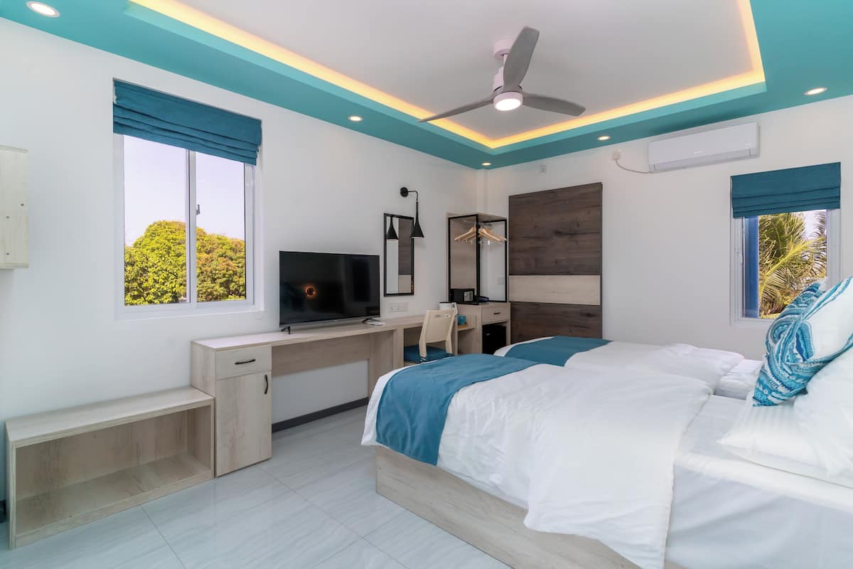 Un dormitorio moderno con cama, escritorio, televisor y ventanas amplias.