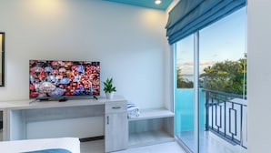 Une chambre moderne dotée d’une grande télévision, d’un petit bureau, d’un banc et d’un balcon avec vue.