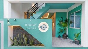 Une entrée d’immeuble avec une façade de couleur turquoise, un escalier et des plantes en pot.