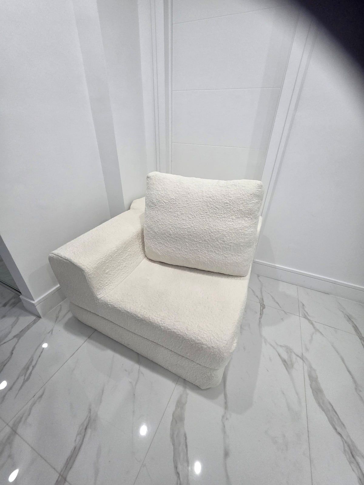 Et hjørne af et rum med en hvid, struktureret sofa op ad væggen, et marmorgulv og en hvid dør.