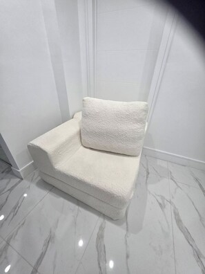 Et hjørne af et rum med en hvid, struktureret sofa op ad væggen, et marmorgulv og en hvid dør.