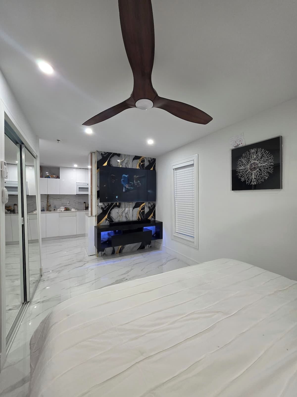 Une chambre moderne avec un ventilateur de plafond, un lit, une télévision et un sol en marbre.