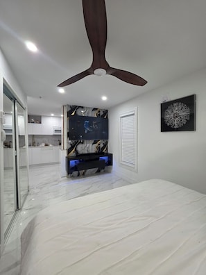 A modern bedroom with a ceiling fan, a bed, a TV, and a marble floor.
