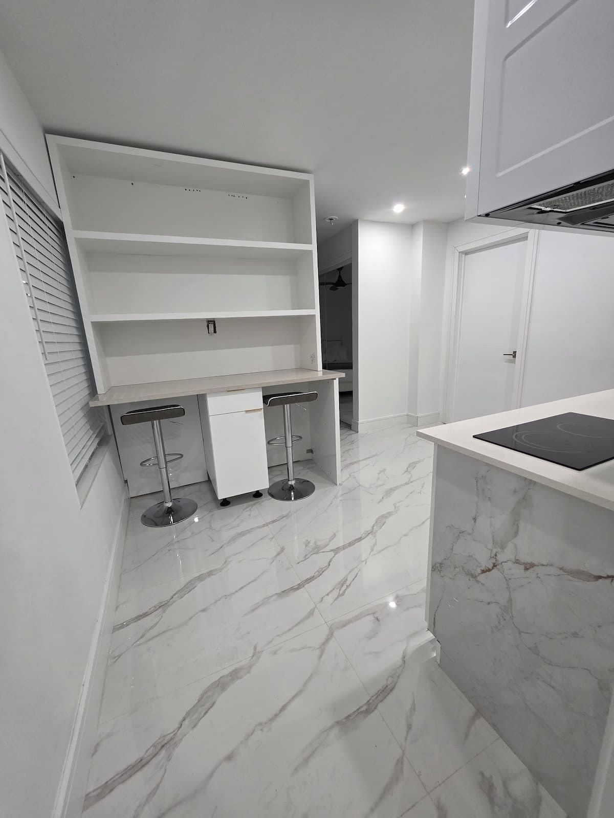 A modern kitchen with a marble countertop, built-in shelves, and a bar area with stools.