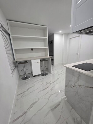 A modern kitchen with a marble countertop, built-in shelves, and a bar area with stools.