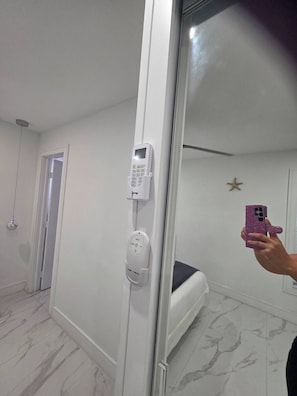 A hotel room with a bed, a bedside table, a mirror, and a door leading to another room.