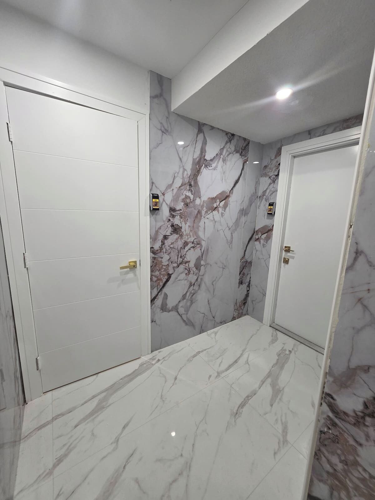 A room with white doors, marble walls, and a marble floor.