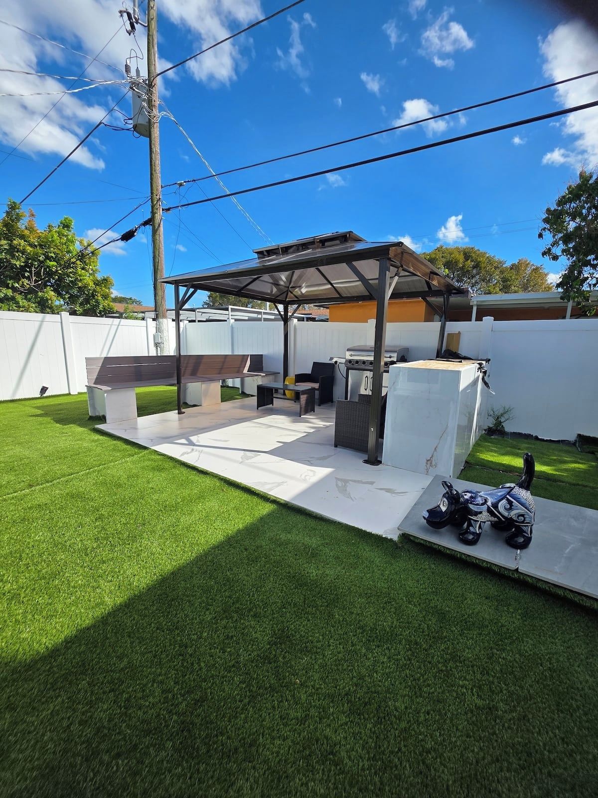 A backyard with a covered patio area, a grill, and a decorative horse statue.