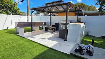 A backyard with a covered patio area, a grill, and a decorative horse statue.