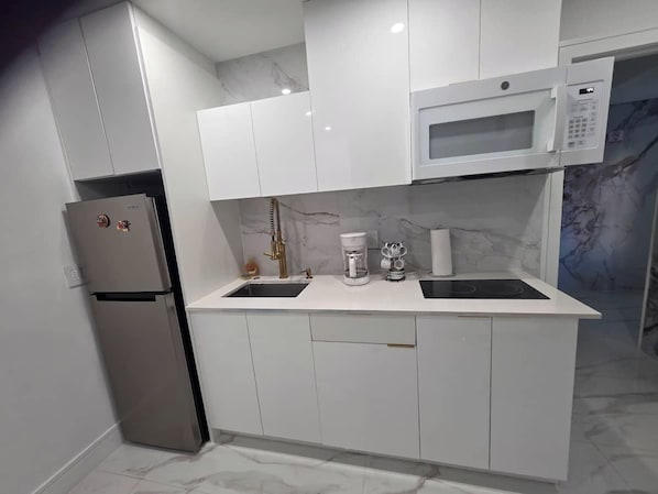 A modern kitchen with white cabinetry, a built-in microwave, a stainless steel refrigerator, and a coffee maker.