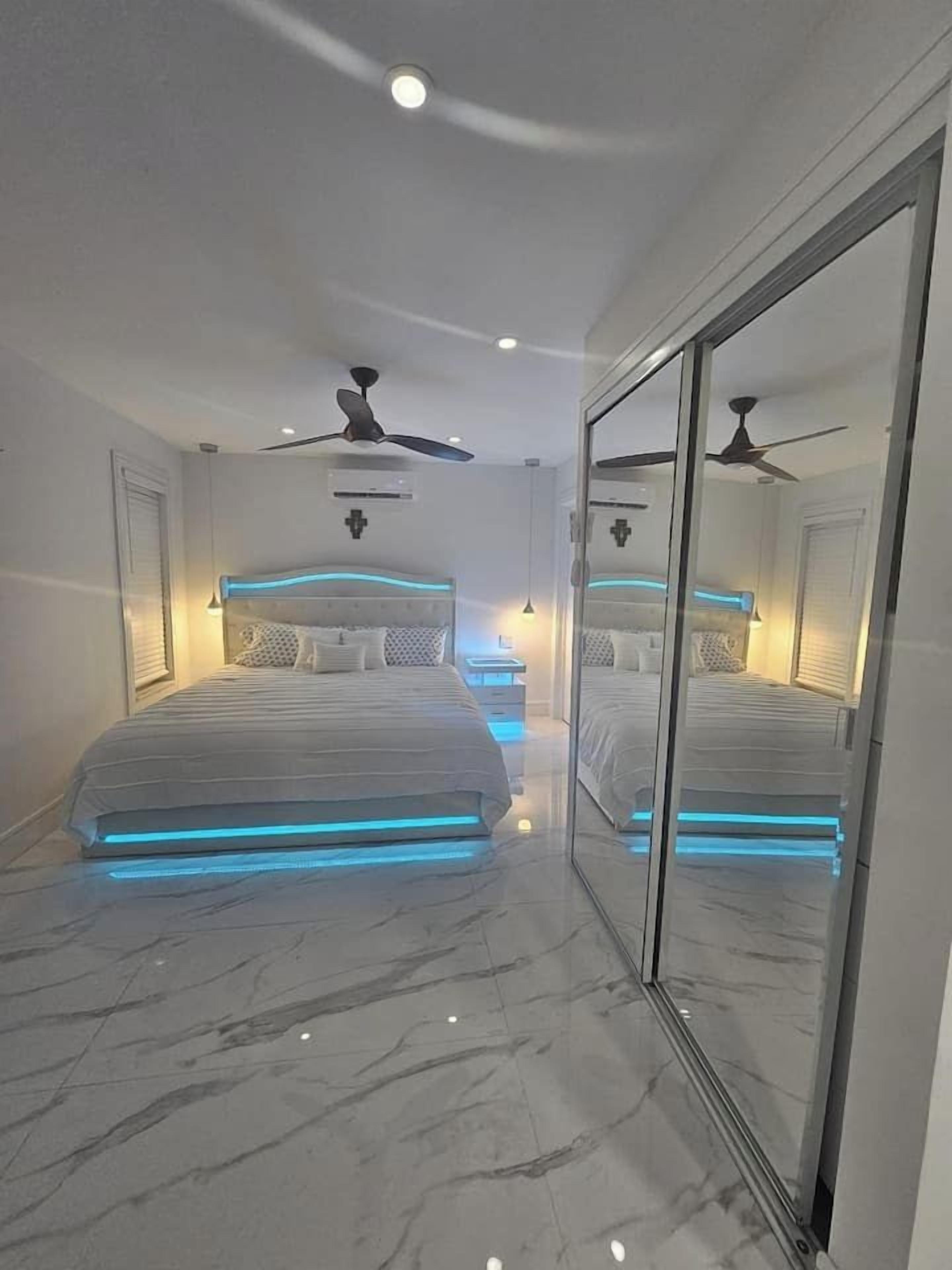 A modern bedroom with two beds, a glass partition, ceiling fans, and recessed lighting.