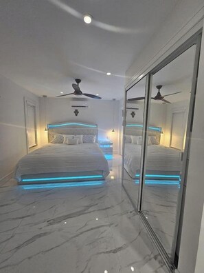 Une chambre moderne avec deux lits, une cloison en verre, des ventilateurs de plafond et un éclairage encastré.