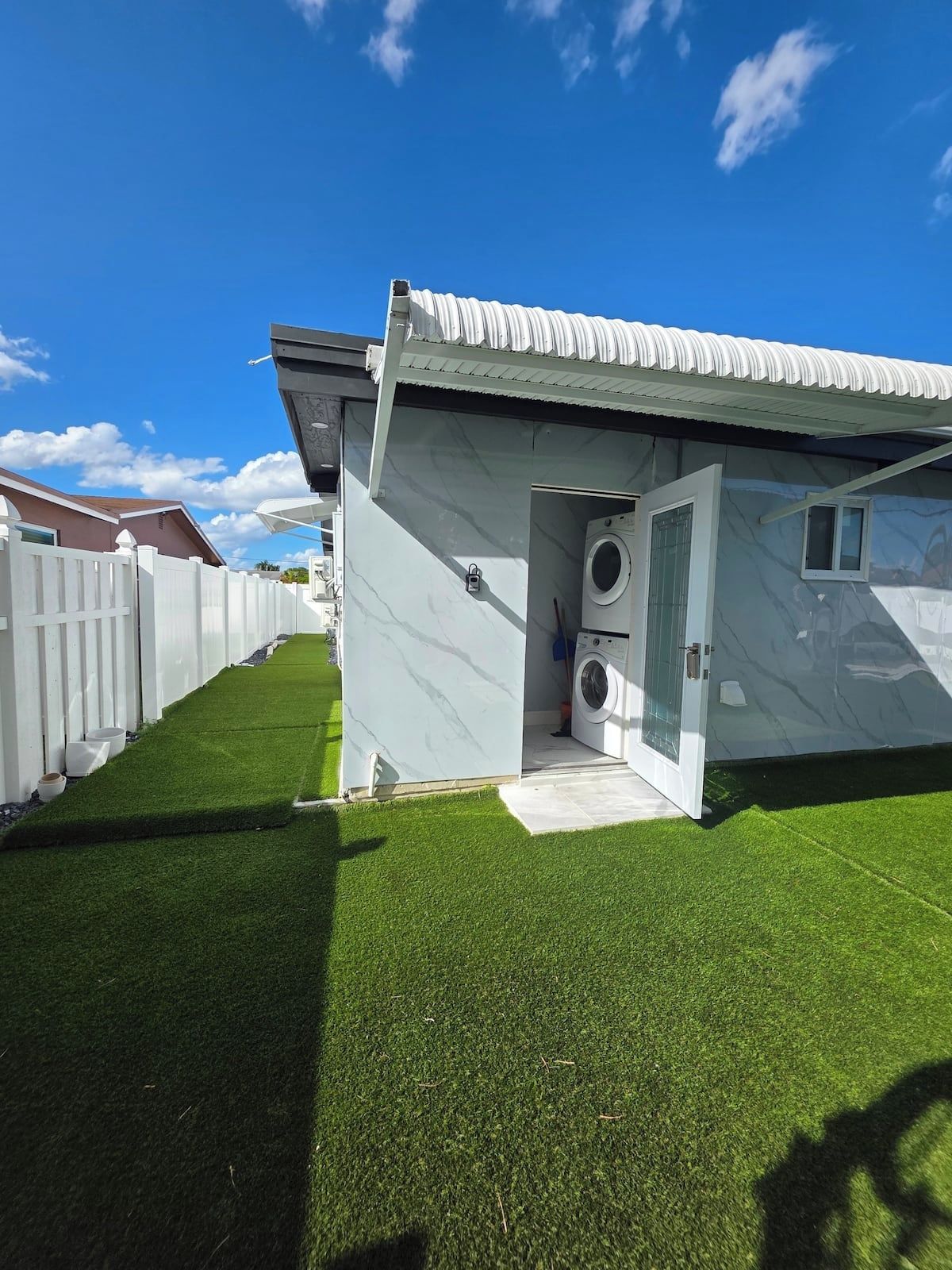 A residential property with a laundry room, a white fence, and artificial grass.
