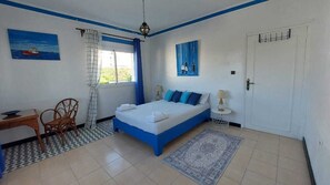 A bedroom with a bed, a desk, a chair, a window with curtains, a door, and a painting on the wall. - Welcoming 5-bedroom bed & breakfast in charming Ksar Sghir Fahs Anjra (Ksar Sghir Fahs Anjra)