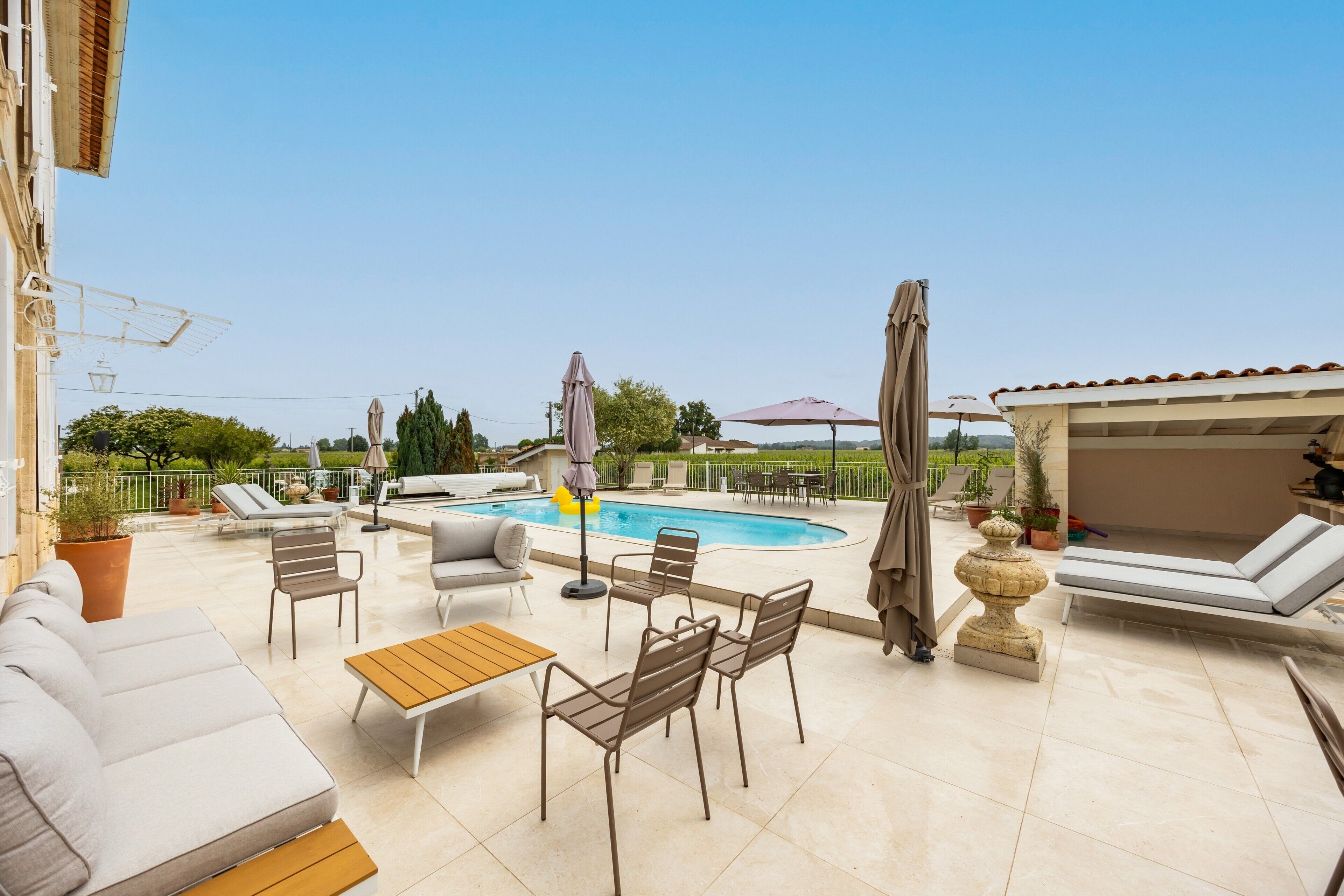 Un espace aménagé au bord de la piscine, avec des chaises longues, une table et des parasols.
