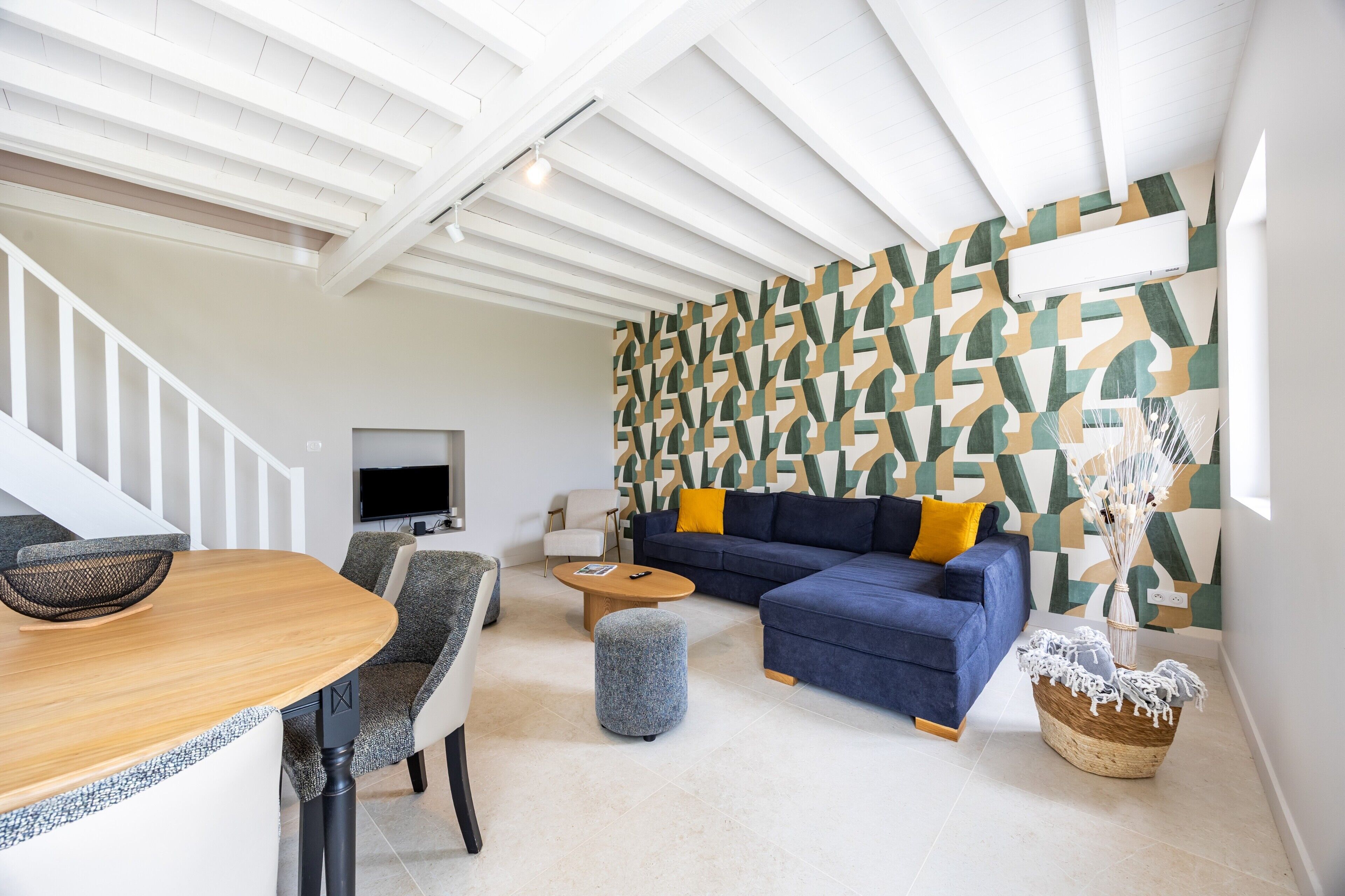 Een moderne woonkamer met een modulaire bank, een ronde salontafel, een eettafel met stoelen en een trap.