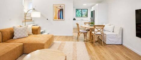 Een moderne woonkamer met een bank, een rond bijzettafeltje, en een eethoek met stoelen en een tafel.