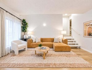 A living room with a sectional sofa, a coffee table, a side chair, a staircase, and a plant. - Relaxed Coastal Stay in Burleigh Heads (Gold Coast)