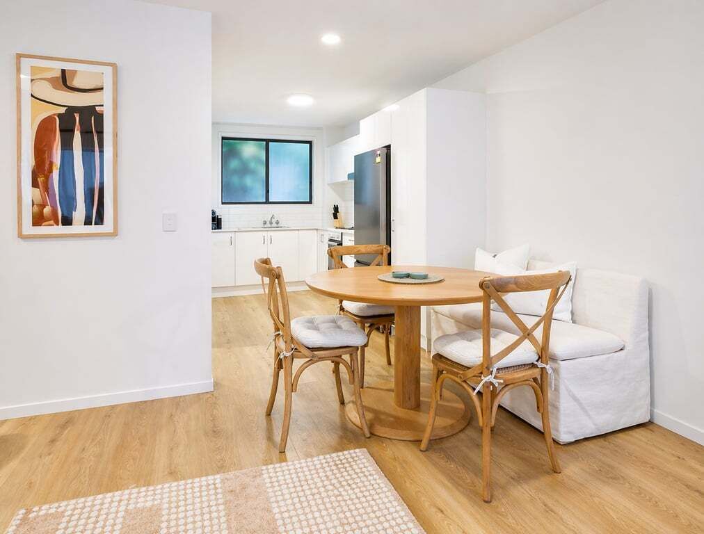 A modern kitchen with white cabinets, a wooden dining table, wicker chairs, and a white sofa.
