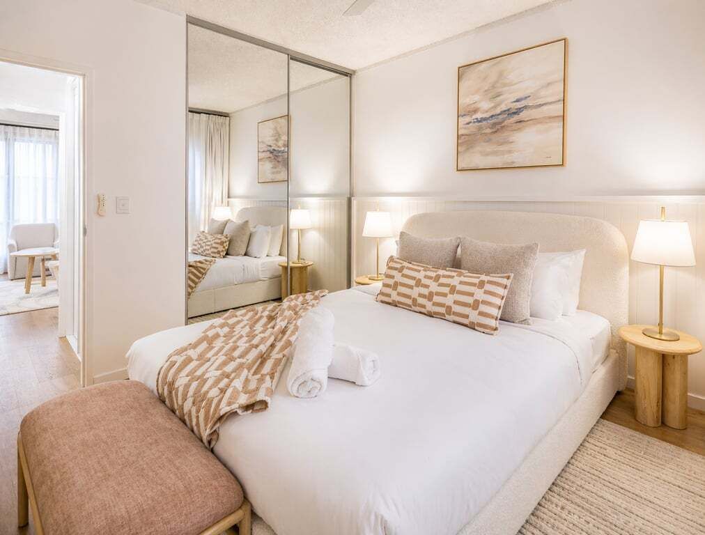 A hotel room with a large bed, bedside lamps, a mirror, and a painting on the wall.