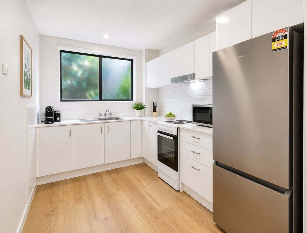A modern kitchen with white cabinets, a stainless steel refrigerator, a microwave, and a window with a view of greenery.