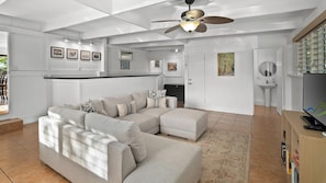 Ein modernes Wohnzimmer mit Ecksofa, Deckenventilator, Küchenzeile und Fernseher.