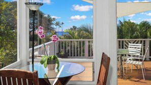 Ein Balkon mit Glastisch, Stühlen, Topfpflanzen und Blick auf Palmen und das Meer.