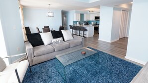 Un salon moderne avec un canapé gris, une table basse en verre et un tapis bleu à motifs.