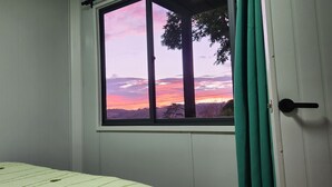 A room with a bed, a window with a view of a sunset, and a door with a curtain. - Los Lirios 2 Cabin (Monteverde)