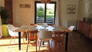 A dining area with a table set for six, surrounded by chairs, a potted plant, and a view through a glass door.