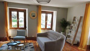 A living room with a sofa, a chair, a small table, a patterned rug, and a bookshelf.