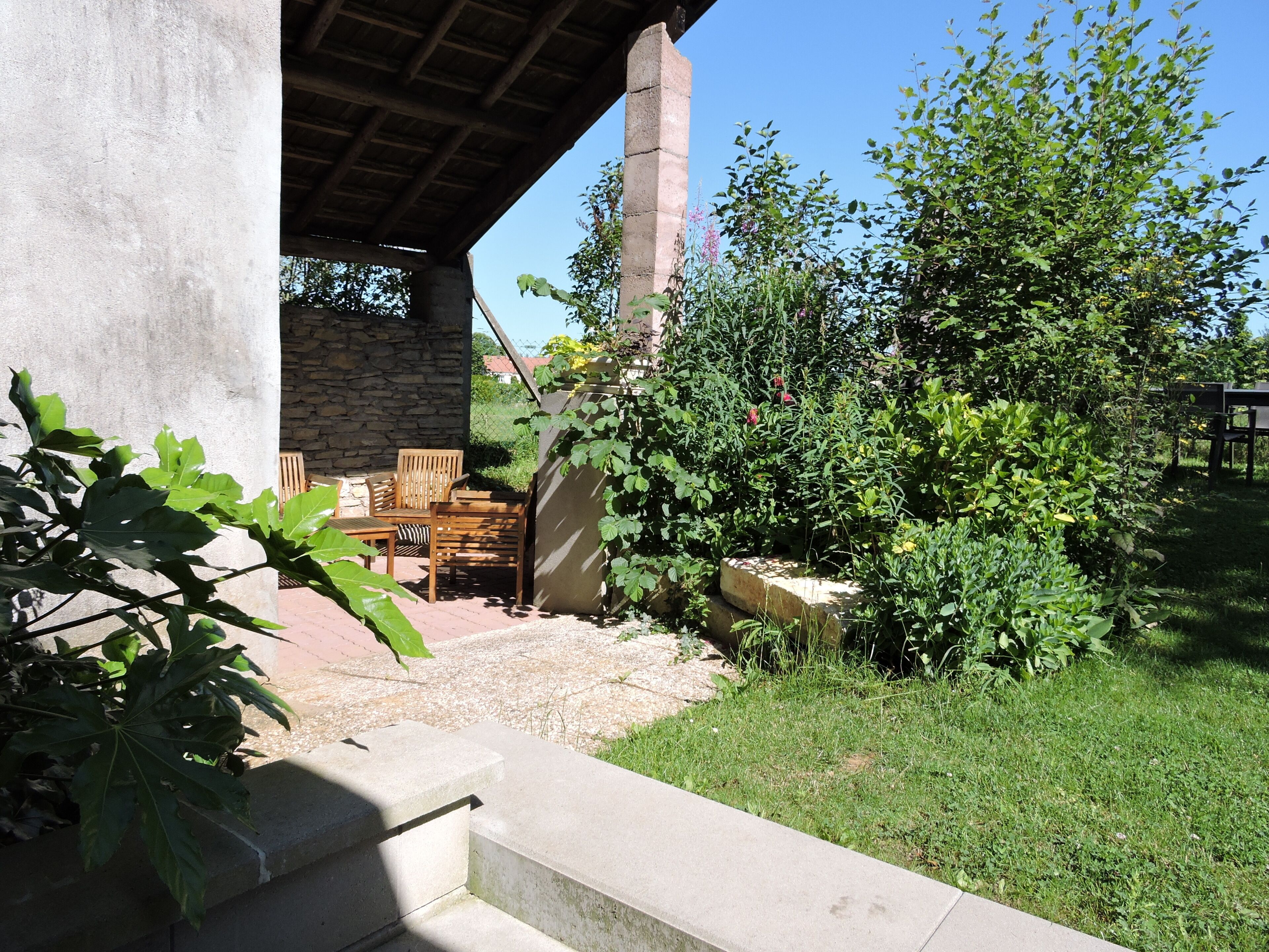 Un espace patio aménagé avec du mobilier d’extérieur, un mur en pierre et un jardin où poussent différentes espèces de plantes.