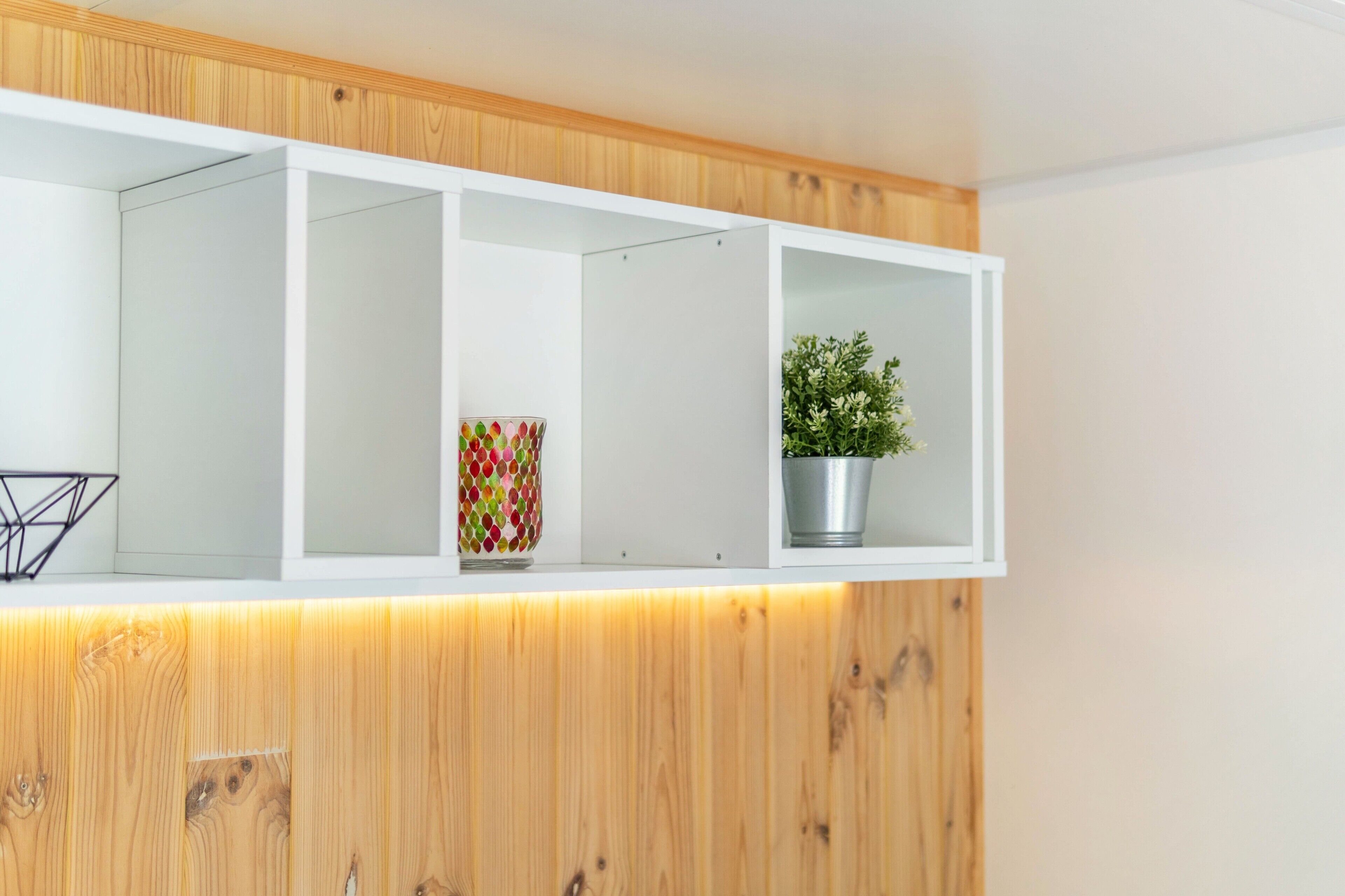 A white shelf with a geometric vase and a potted plant.