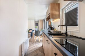 A modern kitchen with a black countertop, wooden cabinets, a built-in oven, and a window with blinds. - Apartment 'Holiday Home Tiny Haus Sunside' with Shared Terrace, Private Garden and Wi-Fi (Riedenburg)