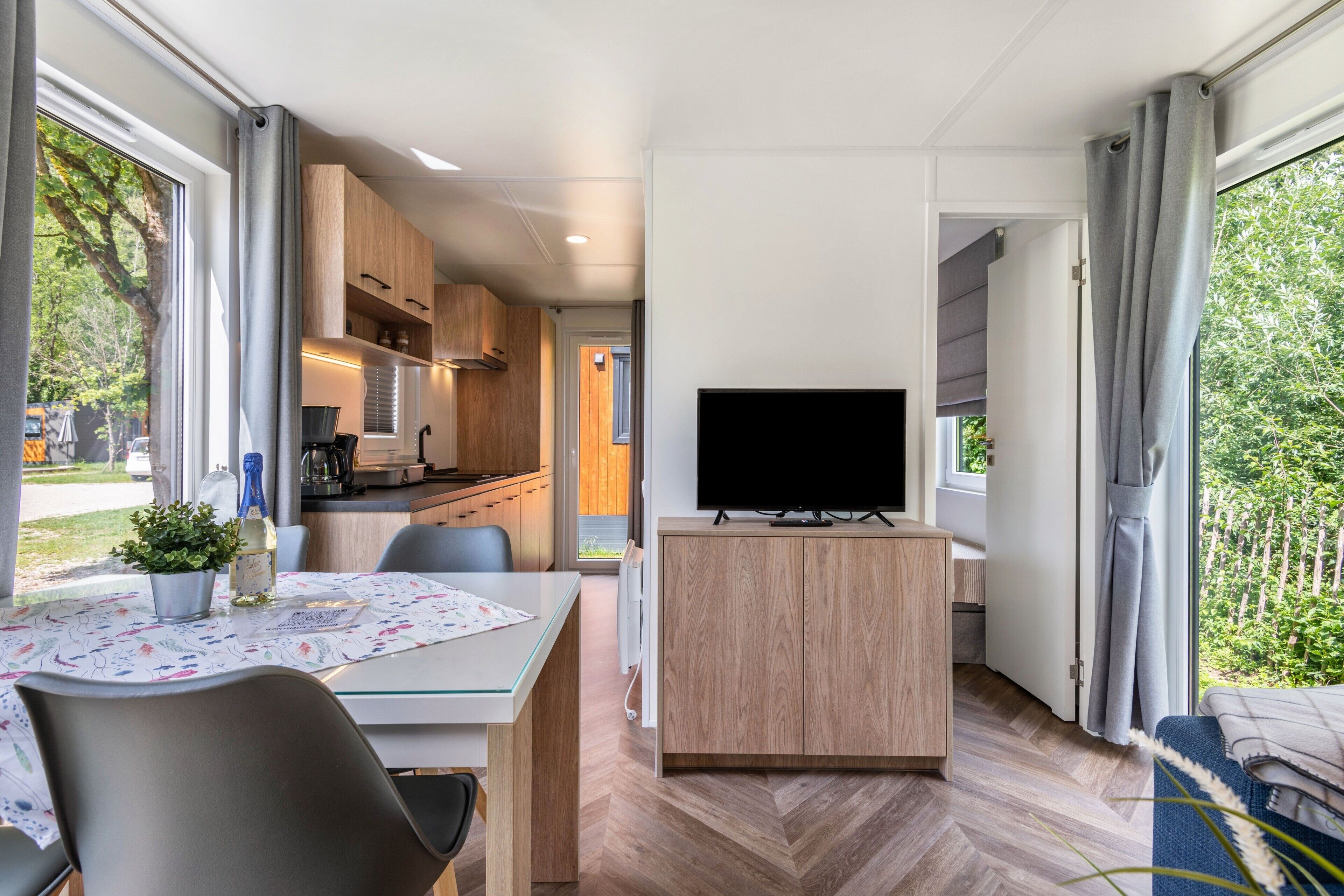 Ein modernes Zimmer mit Esstisch, Stühlen, einem Fernseher auf einem Holzständer und Blick ins Freie.