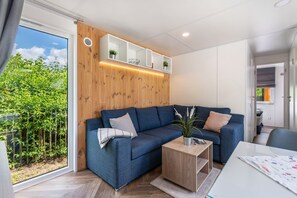A modern living room with a blue sofa, a wooden coffee table, and a built-in shelf with plants. - Apartment 'Holiday Home Tiny Haus Sunside' with Shared Terrace, Private Garden and Wi-Fi (Riedenburg)