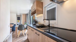 A modern kitchen with wooden cabinets, a black countertop, and a window with blinds.