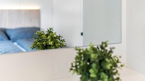 A modern room with a white wall, a large mirror, and a small green plant on the counter.