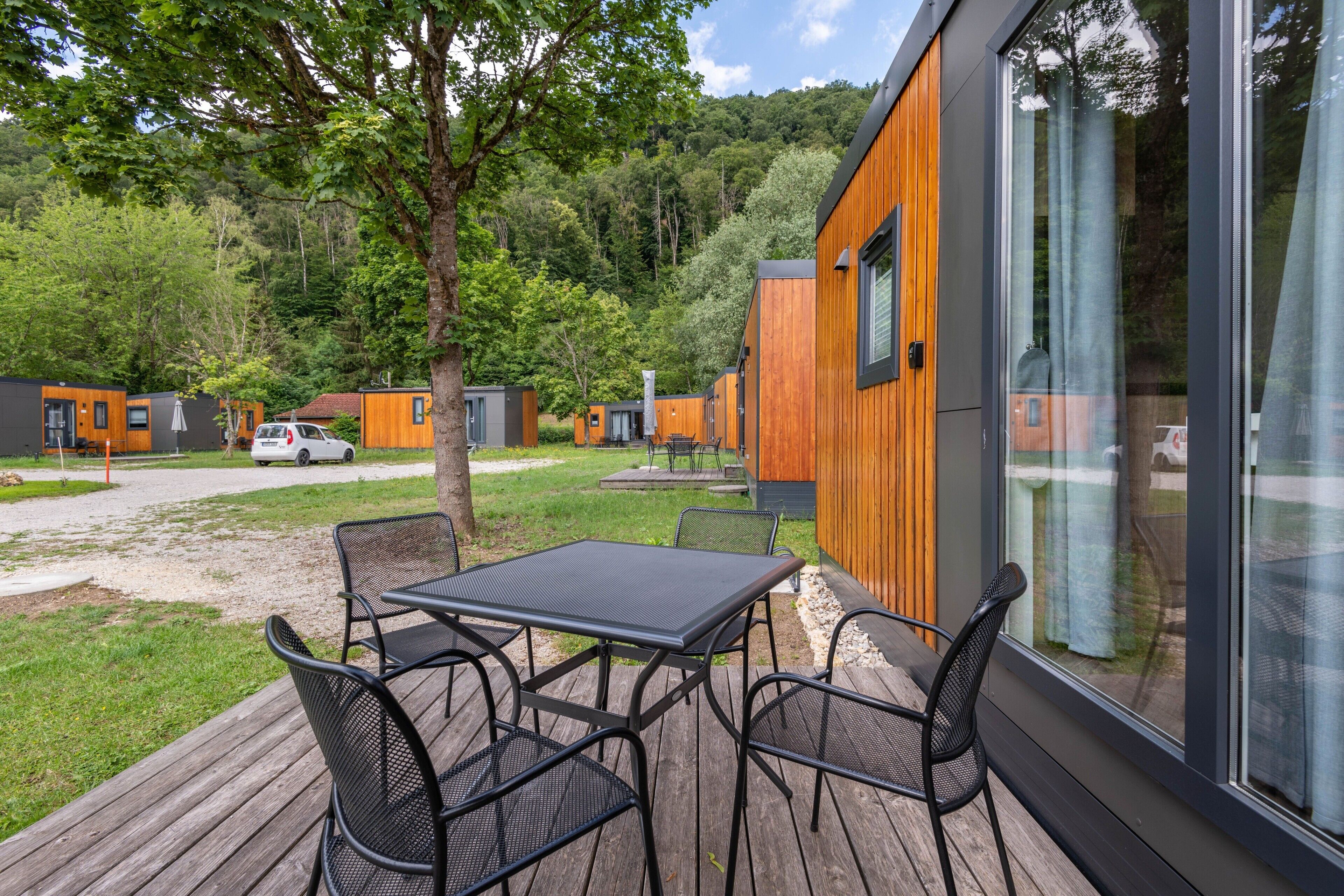 Una terraza moderna al aire libre con una mesa y sillas, rodeada de cabañas de madera con ventanas amplias.