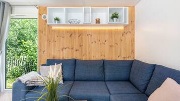 En moderne stue med en blå sofa, træpaneler og et vindue med udsigt til grøn vegetation.