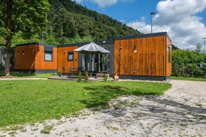 A modern wooden building with a patio area, outdoor seating, and a view of a forested hillside. - Apartment 'Holiday Home Tiny Haus Sunside' with Shared Terrace, Private Garden and Wi-Fi (Riedenburg)