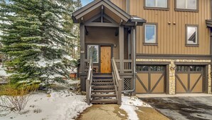 Un bâtiment à deux étages avec une porte d’entrée en bois, un escalier menant à l’entrée et un garage avec des portes marron.