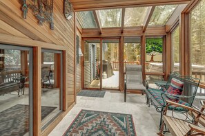 Ein Wintergarten mit Holzwänden, einer Glastür, die nach draußen führt, und einer Sitzecke mit einem gemusterten Teppich.