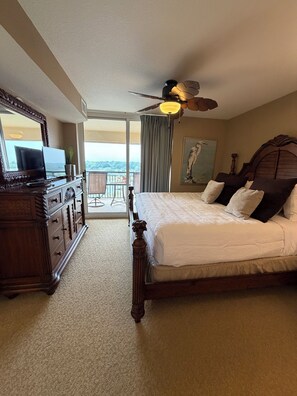Habitación de hotel con cama, cómoda, ventilador de techo, un cuadro y balcón con vistas.