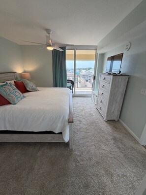 Quarto com cama, cômoda, ventilador de teto e varanda com vista.