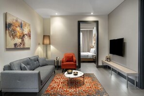 Ein modernes Wohnzimmer mit grauem Sofa, einem roten Sessel, einem Couchtisch, einem Flachbildfernseher und einem Gemälde an der Wand.