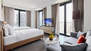 A hotel room with a bed, a TV, a sofa, a coffee table, and large windows with curtains. - Bomonti Suites (Istanbul)