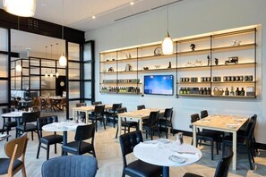 A modern restaurant interior with round tables, black chairs, pendant lighting, and a wall-mounted display of bottles. - Bomonti Suites (Istanbul)
